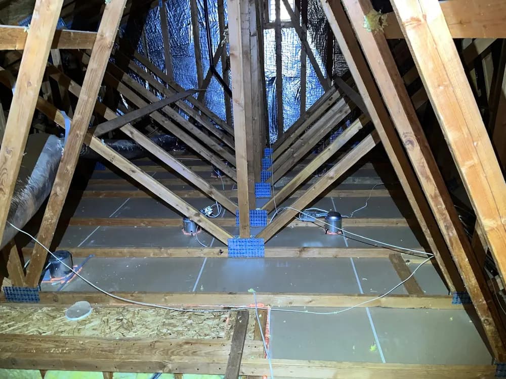 Cleared attic showing bare framing, the drywall ceiling plane below and exposed junction boxes awaiting sealing.