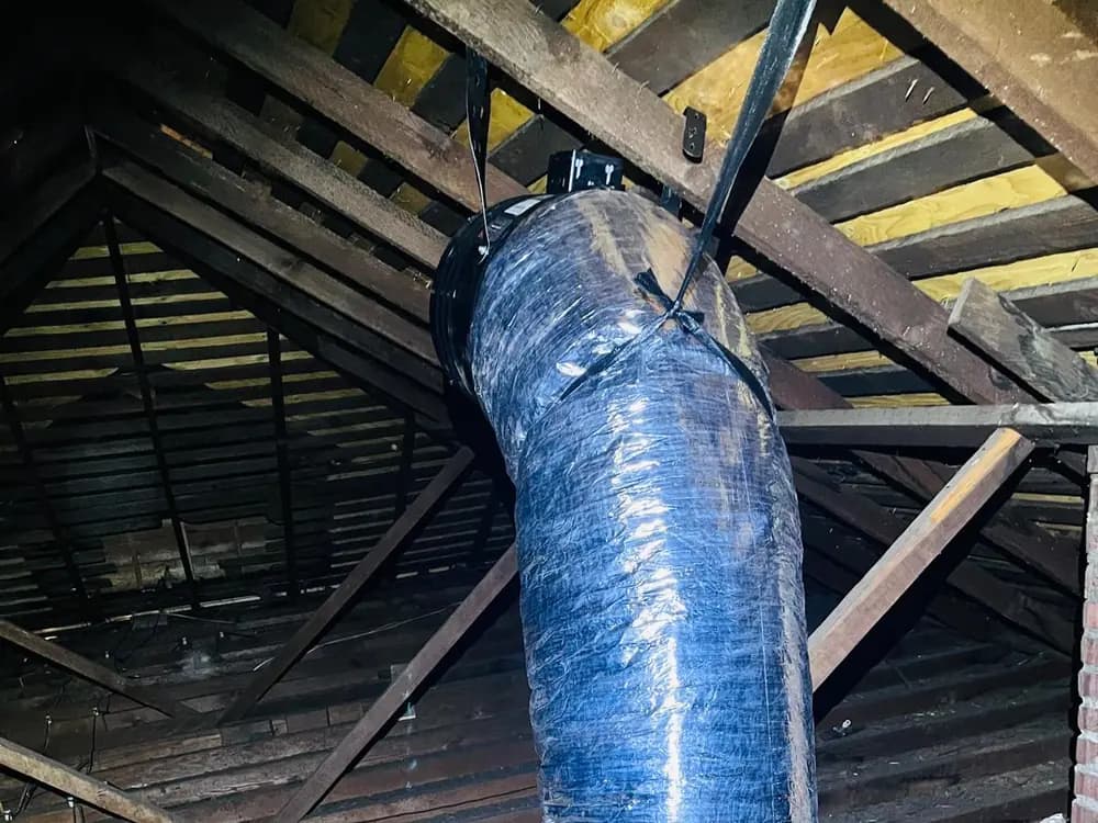 Insulated flexible duct running up through the attic framing to a fan unit at the roof.