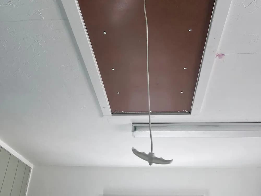 Pull-down attic ladder installed in a ceiling opening with a trimmed and painted surround.