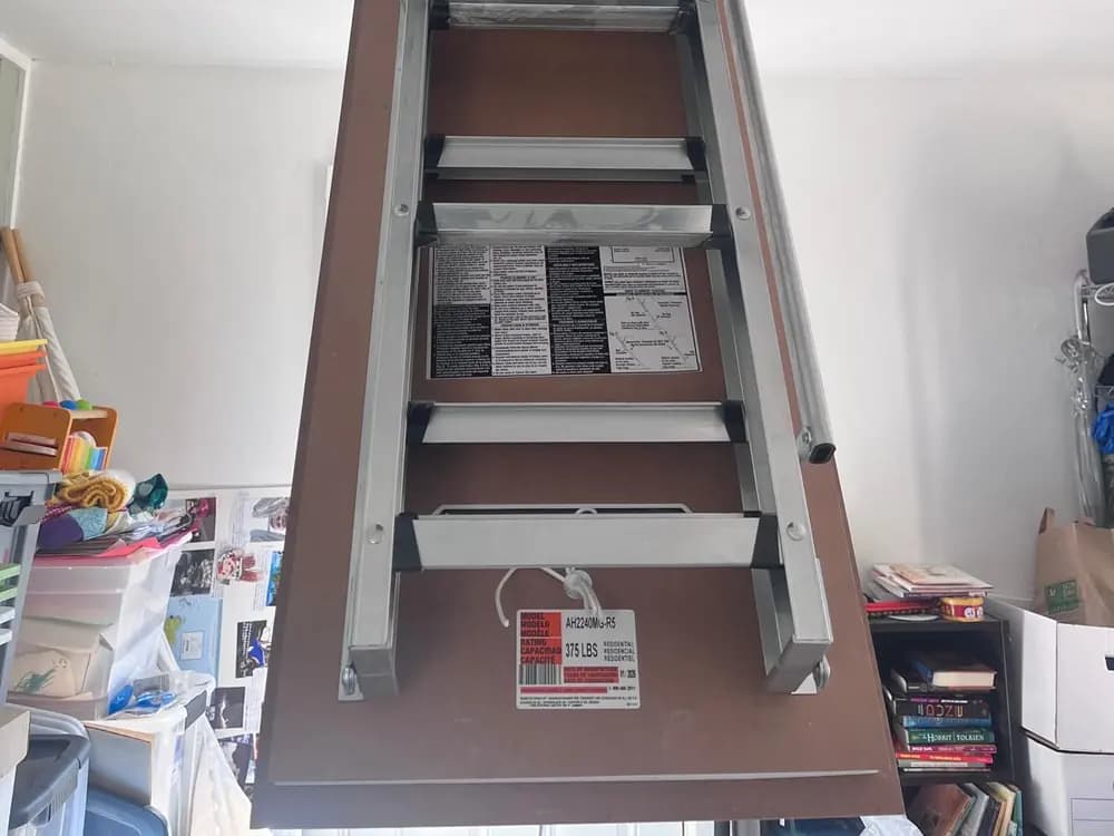 Aluminium attic ladder fully extended from its ceiling door, treads level and the manufacturer rating label fixed to the lower section.