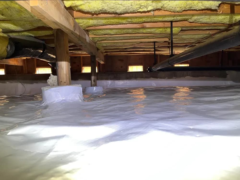 Crawl space con una barrera de vapor sobre el terreno y aislamiento en rollo colocado entre las vigas del piso de arriba.