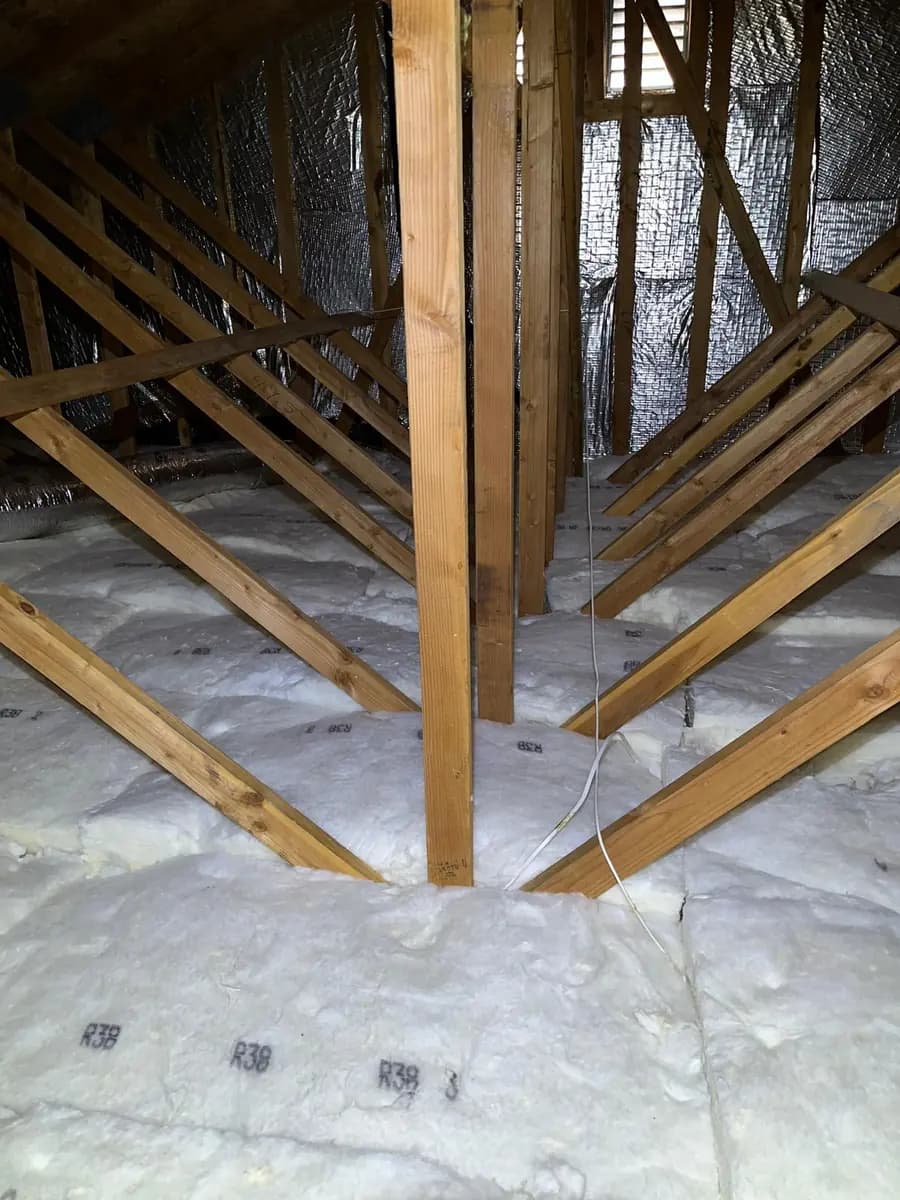 Piso de ático con aislamiento en rollo nuevo colocado de forma pareja entre las vigas y una barrera radiante instalada en las vigas del techo.