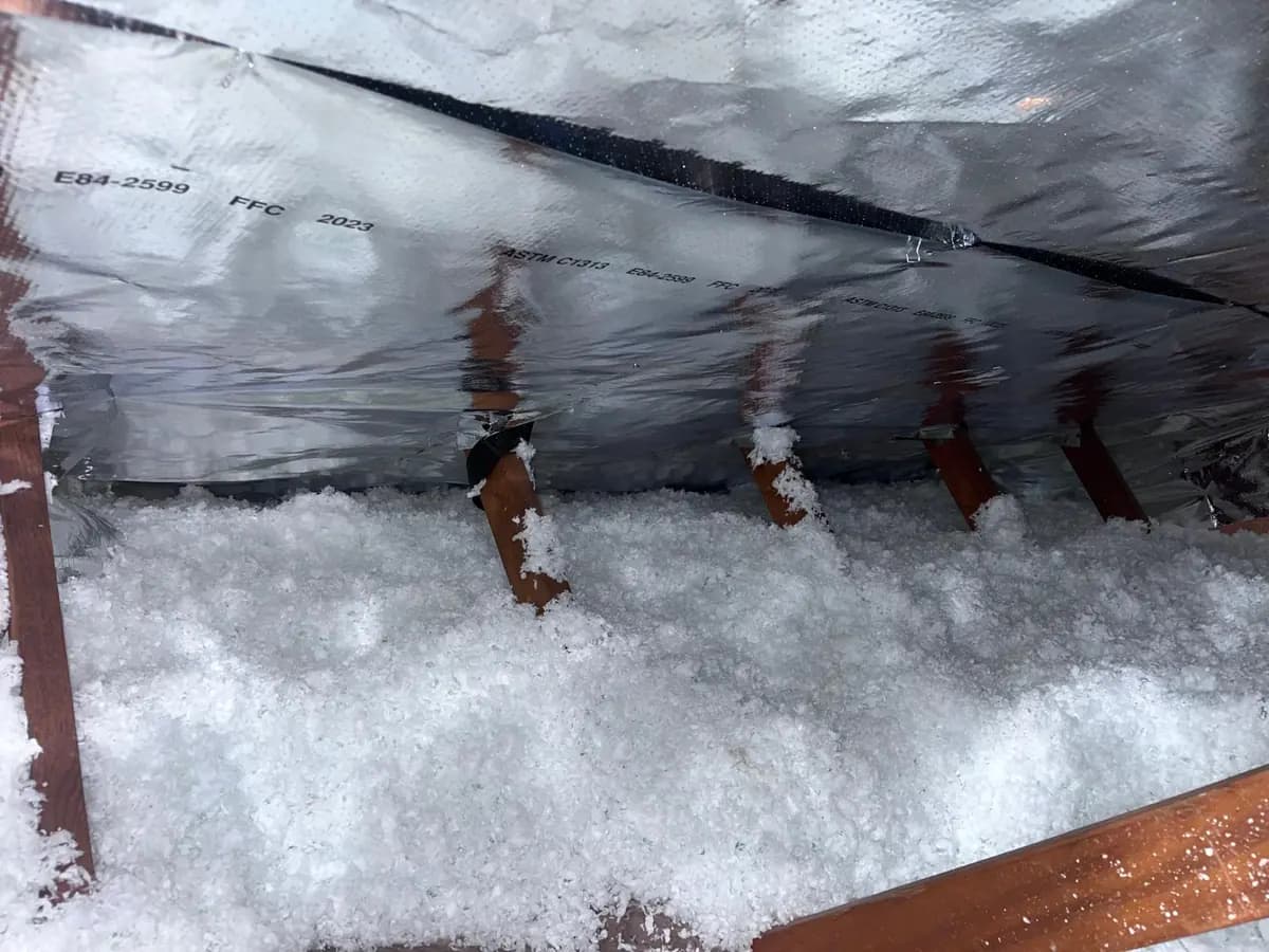 Attic floor covered with an even layer of loose-fill insulation, with a radiant barrier fitted above at the roof line.