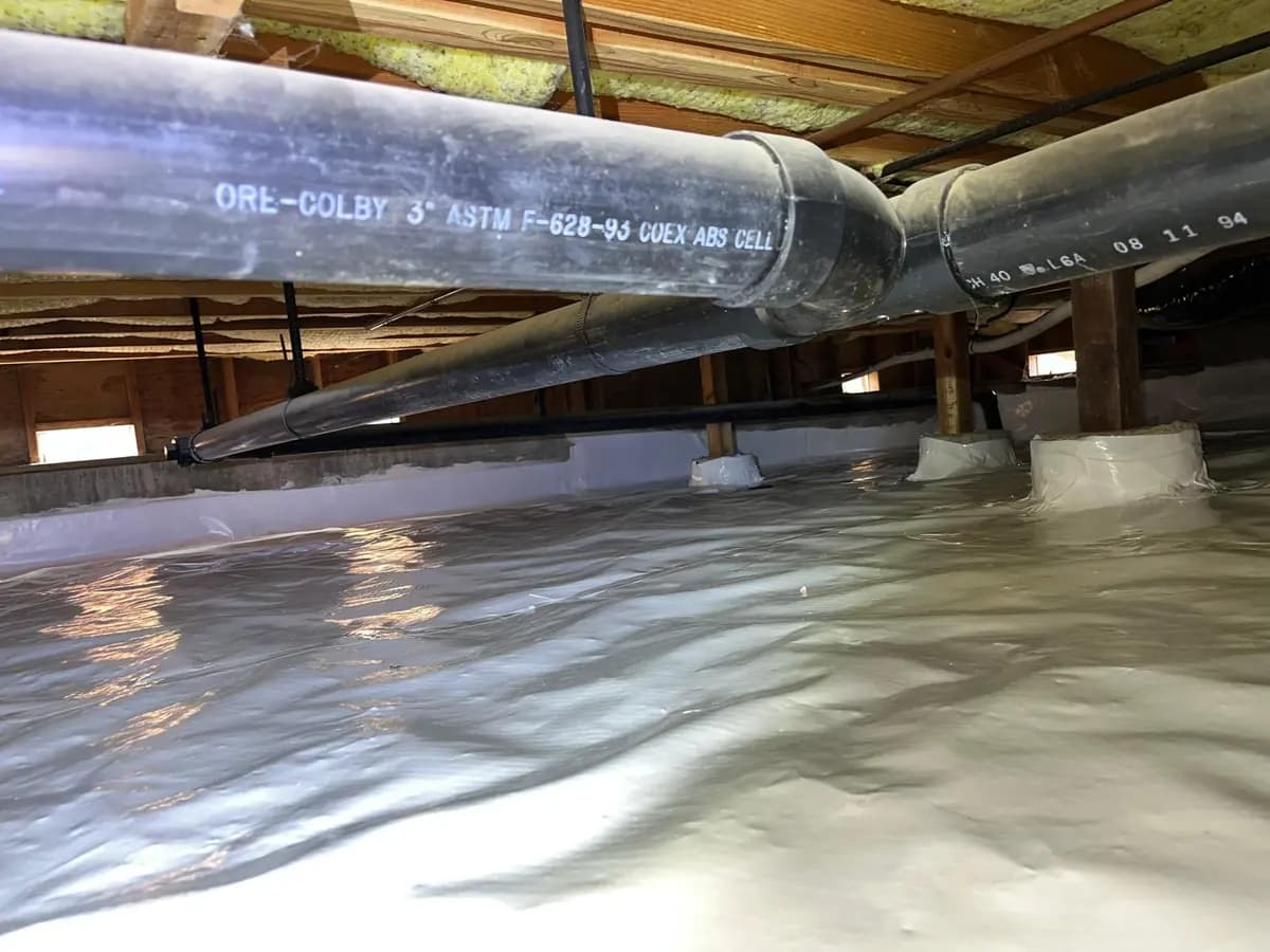 Crawl space with a continuous vapor barrier laid across the ground and sealed around the pier footings.